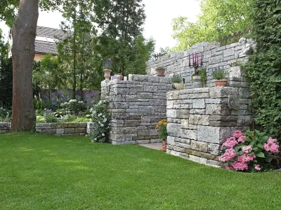 Eine kunstvoll gemauerte Wand aus Naturstein bildet einen idyllischen Rückzugsort im grünen Garten.