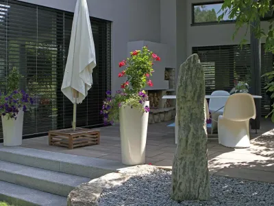 Moderne Terrassengestaltung mit großformatigen Platten, einem Quellstein aus Naturstein und hellen Blockstufen.