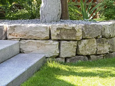 Eine niedrige, geschwungene Trockenmauer aus Naturstein grenzt ein Kiesbeet sauber vom Rasen ab.