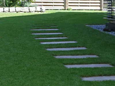In einen dichten Fertigrasen eingelassene Trittplatten als stabiler Laufweg im Hausgarten.