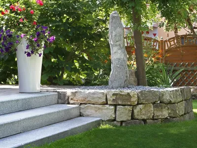 Monolithischer Quellstein auf einer Naturstein-Trockenmauer neben breiten Treppenstufen im Garten.