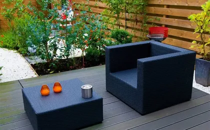 Ein dunkler Rattan-Sessel und Tisch auf einer grauen Holzterrasse im Garten. Stilvolle Terrassen aus Holz zum Entspannen.