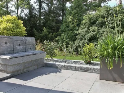 Eine moderne Terrasse aus großen keramischen Platten und einer massiven Sitzbank aus Naturstein.