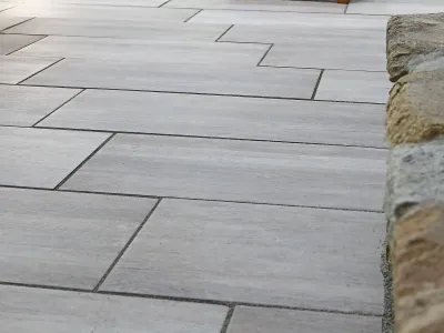 Moderne Platten auf einer Terrasse, sauber verfugt und flankiert von einer Mauer aus Naturstein.