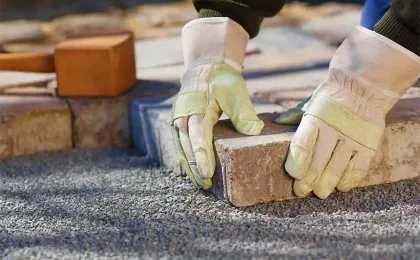 Handwerker mit Schutzhandschuhen setzt Pflastersteine präzise ins Splittbett. Fachgerechte Pflasterarbeiten im Garten.
