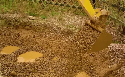 Ein gelber Bagger löffelt steinige Erde bei Erdarbeiten im Garten. Professionelle Baggerarbeiten für Fundamente.