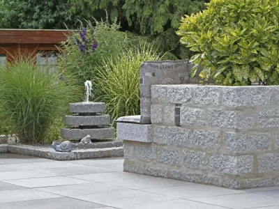 Moderne Terrasse aus Keramikplatten kombiniert mit einer gemauerten Bank aus Granit-Naturstein.