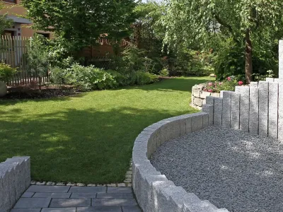 Ein gepflegter Hausgarten mit geschwungenen Steinpalisaden, Splittbett und dichter Rasenfläche.