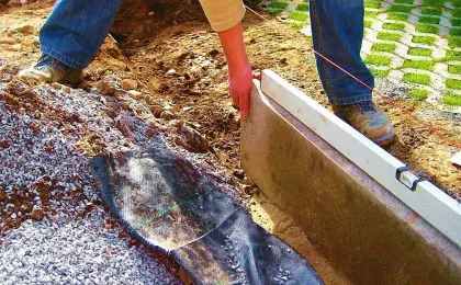 Handwerker richtet eine Kante mit der Wasserwaage aus. Stabile Einfassung für Pflastersteine bei Pflasterarbeiten.