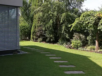 Rechteckige Trittplatten bilden einen geschwungenen Pfad durch den saftig grünen Rollrasen im Hausgarten.