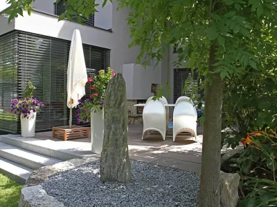 Einladende Terrasse mit stilvollen Gartenmöbeln, umrahmt von edlem Naturstein und schattenspendenden Bäumen.