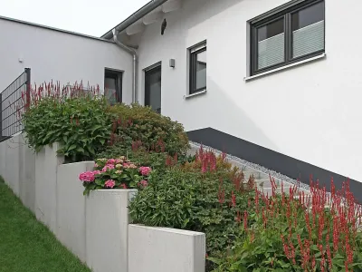 Abgestufte Winkelstützwand fängt die Böschung am Haus sicher ab und schafft Platz für Blumenbeete.
