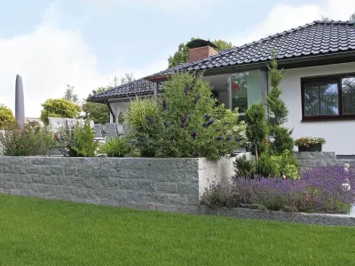 Ein mit duftendem Lavendel bepflanztes Hochbeet aus hellen Naturstein-Blöcken auf einer Rasenfläche.