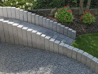 Eine geschwungene Rampe mit einer robusten Palisadeneinfassung aus grauem Naturstein im Garten.