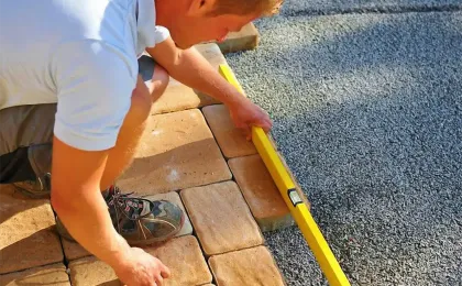Ein Landschaftsgärtner prüft das frisch verlegte Pflaster mit einer gelben Wasserwaage auf exakte Ausrichtung.