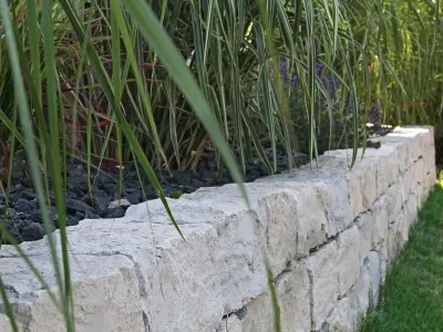 Detailansicht einer massiven Trockenmauer aus Jurakalk-Naturstein entlang einer Rasenfläche.