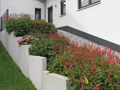 Abgestufte Mauerscheiben fangen den Hang ab und bieten Platz für üppige Gartengestaltung & Gartenpflege.