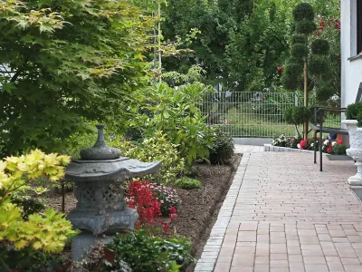 Harmonische Vorgartengestaltung mit einem Pflasterweg, dichten Sträuchern und einer Steinlaterne.
