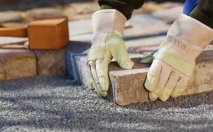 Handwerker mit Schutzhandschuhen setzt Pflastersteine präzise ins Splittbett. Fachgerechte Pflasterarbeiten im Garten.