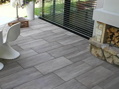 Moderne Terrasse aus Keramikplatten in Holzoptik mit einer gemauerten Kaminbasis aus Naturstein.