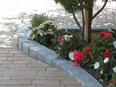 Eine geschwungene Beeteinfassung aus kleinen Pflastersteinen grenzt ein buntes Blumenbeet ab.