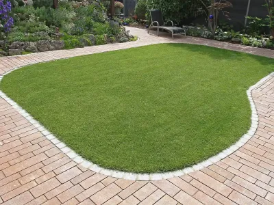 Eine saftig grüne Rasenfläche, sauber eingefasst mit hellen Pflastersteinen im Hausgarten.