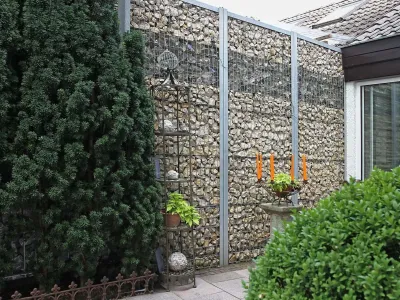 Moderne Gabionenwand gefüllt mit hellem Naturstein als stabiler Sichtschutz im Gartenbereich.