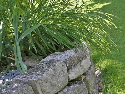 Üppig blühendes Hochbeet aus Naturstein direkt an einer gepflegten Rasenfläche im Garten.