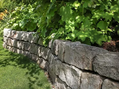 Geschwungene Naturstein-Trockenmauer als stabile Beeteinfassung neben einer gepflegten Rasenfläche.