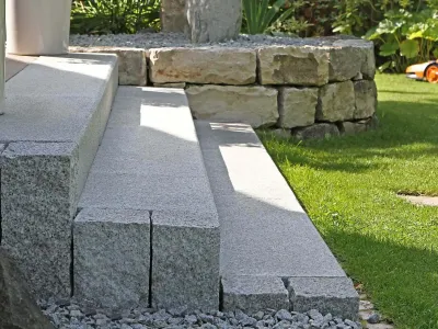 Präzise gesetzte Blockstufen aus grauem Naturstein als Treppeneinfassung entlang des Rasens.