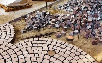 Traditionelle Natursteinarbeiten auf Sandbett. Rötliche Pflastersteine aus Naturstein werden im Bogen verlegt.