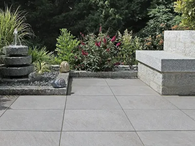 Elegante Terrasse aus Naturstein mit einem plätschernden Brunnen und einer massiven Steinbank.