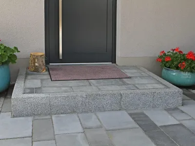 Ein stabiles Eingangspodest eingefasst mit edlem Naturstein für einen einladenden Hauseingang.
