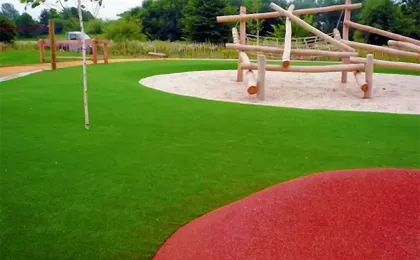 Robuster Kunstrasen auf einem öffentlichen Spielplatz mit Holz-Klettergerüst. Sicherer künstlicher Rasen für Kinder.