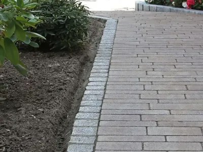 Exakte Pflasterarbeiten für einen geschwungenen Fußweg aus robusten Pflastersteinen im Garten.