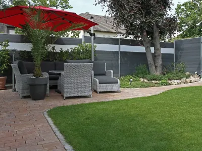 Ein gemütlicher Sitzplatz im Garten mit modernen Zäunen als Sichtschutz und sauberen Pflasterarbeiten.