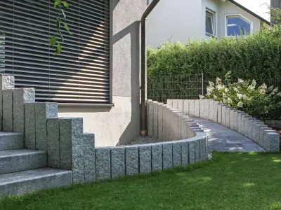 Robustes Mauerwerk und Stufen aus grauem Naturstein fangen den Hang sauber neben dem Rasen ab.