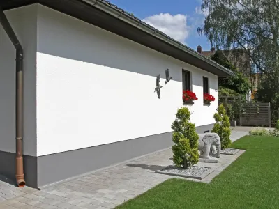 Saubere Pflasterarbeiten mit Pflastersteinen entlang einer Hauswand und einer dichten Rollrasenfläche.