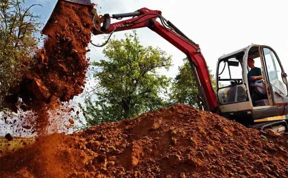 Ein roter Kettenbagger schüttet einen großen Haufen braune Erde auf. Kraftvolle Baggerarbeiten bei den Erdarbeiten.