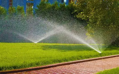 Zwei Versenkregner bewässern gleichzeitig eine große Rasenfläche neben einem Pflasterweg. Moderne Gartenbewässerung.
