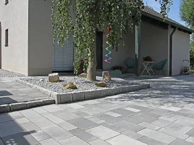 Großflächige Pflasterarbeiten für eine moderne Einfahrt mit integriertem Baumbeet und Graniteinfassung.