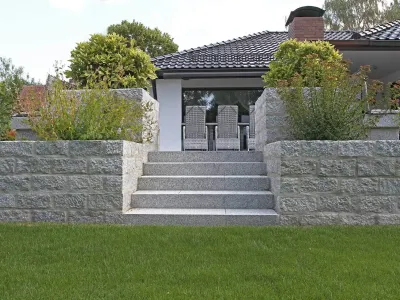 Symmetrische Treppenanlage aus hellem Naturstein flankiert von gemauerten Hochbeeten im Garten.