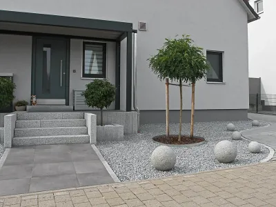 Moderner Eingangsbereich vom Wohnhaus mit Granitelementen und stilvoller Gartengestaltung im Kiesbeet.