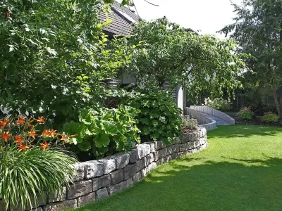 Aufwändige Gartengestaltung mit einer geschwungenen Naturstein-Trockenmauer und einer gepflegten Rasenfläche.