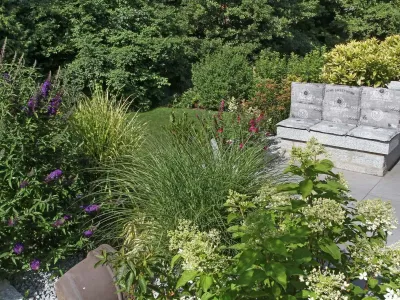 Stilvolle Gartengestaltung mit einer Bank aus Naturstein inmitten prachtvoller Pflanzen.