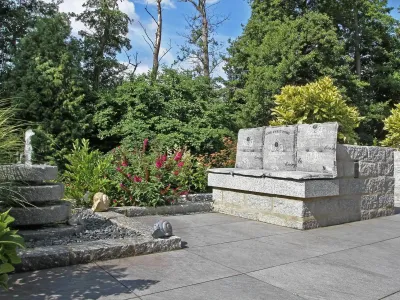 Eine steinerne Gartenbank aus Naturstein direkt neben einem plätschernden Wasserspiel auf der Terrasse.
