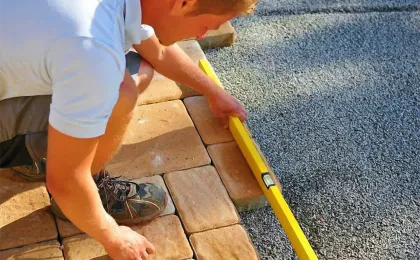 Ein Landschaftsgärtner prüft das frisch verlegte Pflaster mit einer gelben Wasserwaage auf exakte Ausrichtung.